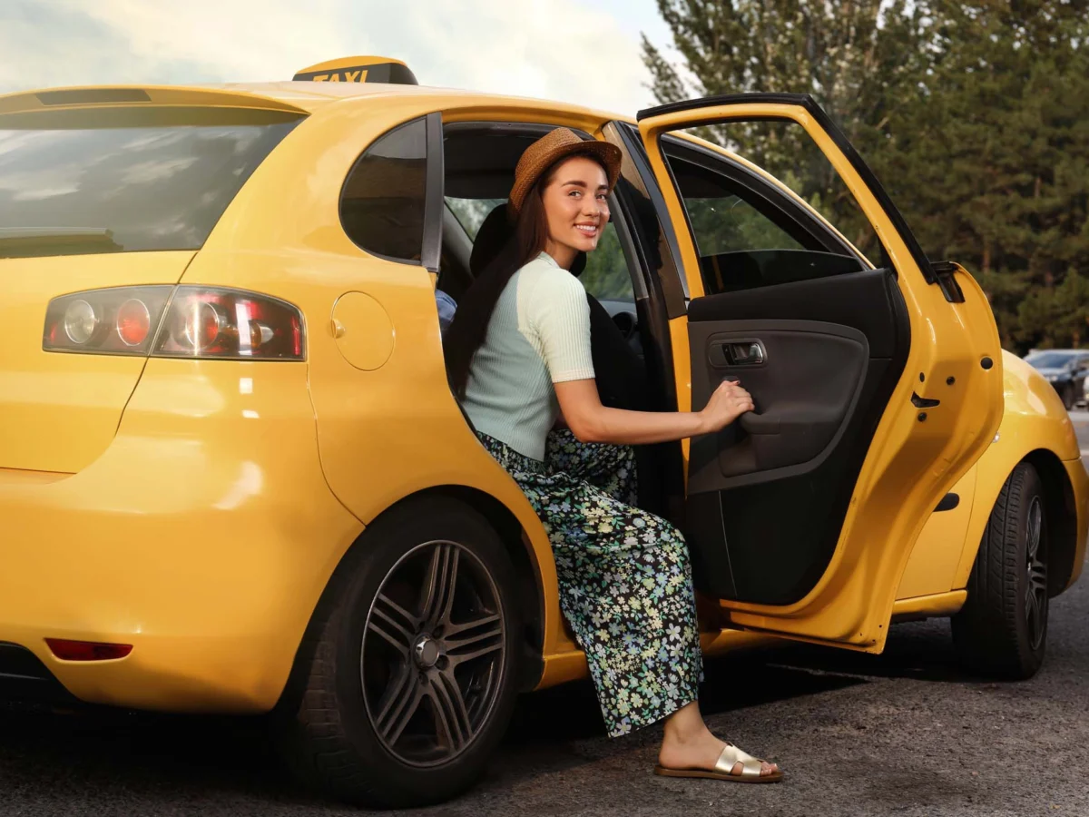 Professional photo of a young woman exiting the back of yellow taxi cab
